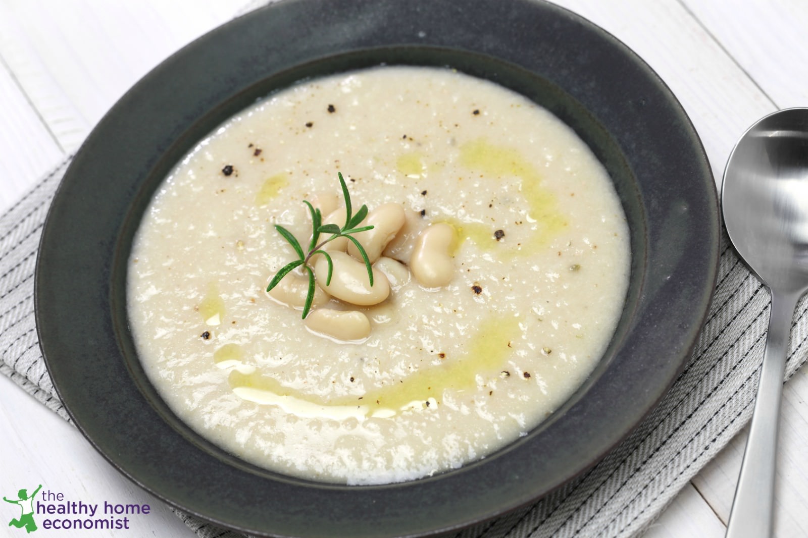 bean and bacon soup in a black bowl with tablecloth and spoon