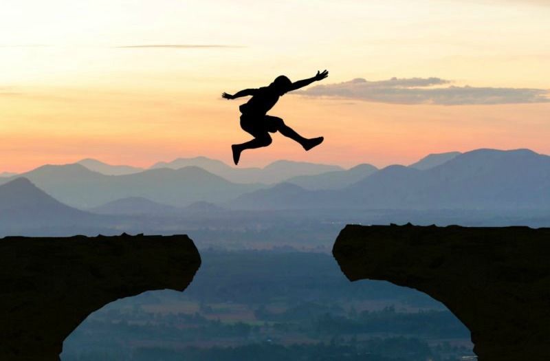 man leaping over a gap in a cliff