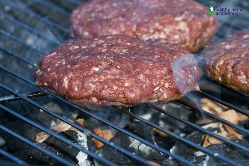 three bison burger patties on a charcoal grill with orange flame