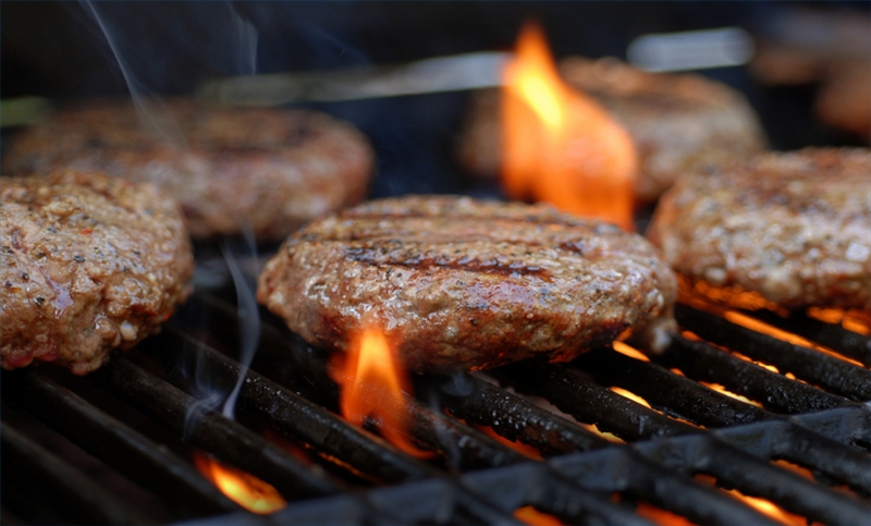 burgers grilling on a charcoal barbecue with a low flame