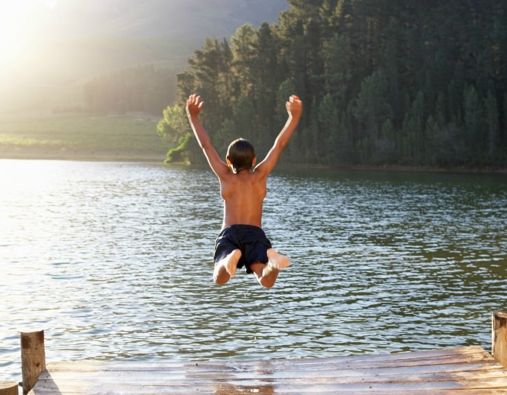 Boy jumping off a dock into a lake for a natural waters swim