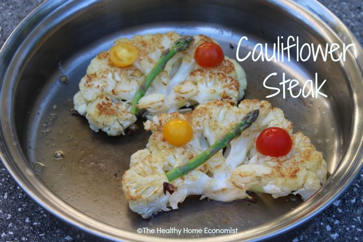 cauliflower steaks in frying pan garnished with asparagus and tomatoes