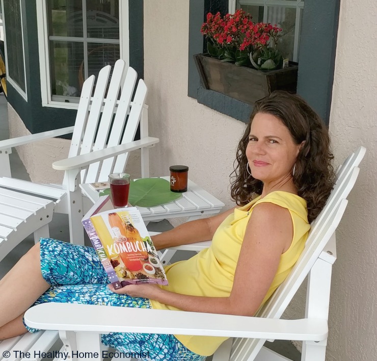 woman reading a book about kombucha myths on a porch in a white chair