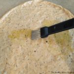 brushing gluten free pizza crust with olive oil