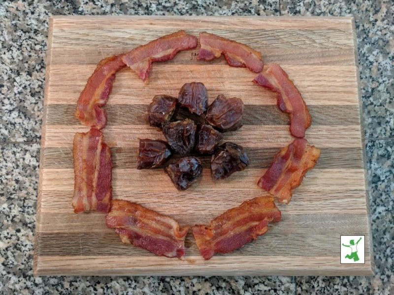 raw dates and cooked bacon slices on a wooden cutting board