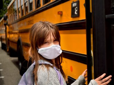 child wearing a mask boarding a school bus