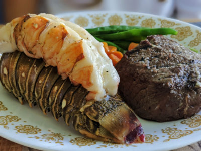 baked lobster tail on a white plate with vegetables