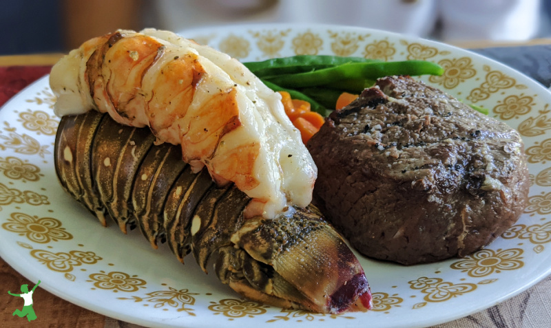 baked lobster tail on a white plate with vegetables