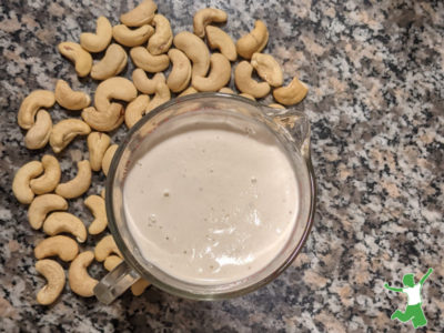 cashew cream in a glass measuring cup with cashews on counter