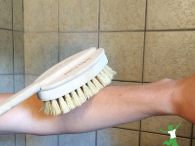 young woman dry brushing her skin in shower