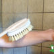 young woman dry brushing her skin in shower