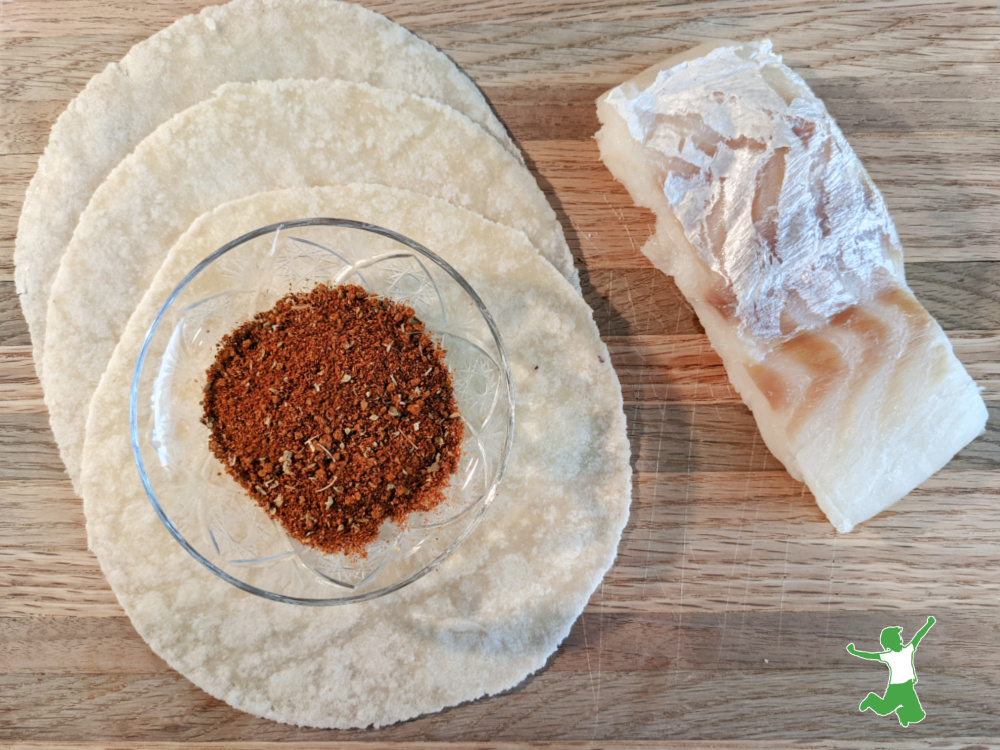 fish taco seasoning in a glass bowl with tortillas and cod fillet