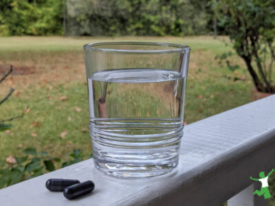 activated charcoal detox capsules and glass of water with natural background
