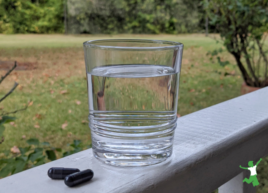 activated charcoal detox capsules and a glass of water on railing natural background