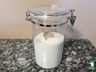 homemade green laundry powder in container with wooden scoop