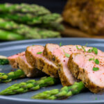 Pork fillet slices on a blue plate with asparagus spears