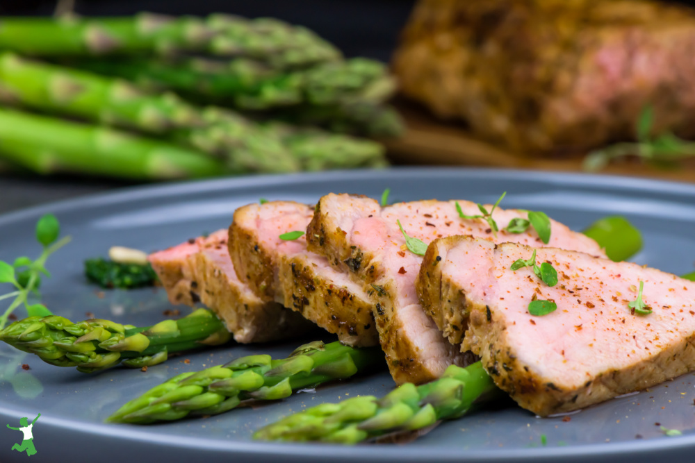 sliced pork tenderloin with asparagus on a blue plate