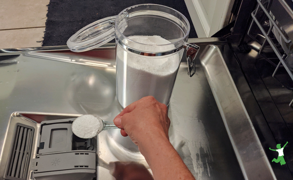 woman adding one tablespoon of homemade dishwasher powder to dispenser