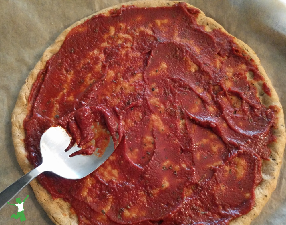healthy keto pizza crust on parchment paper with tomato sauce