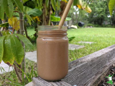 carob banana avocado smoothie in a glass with bamboo straw