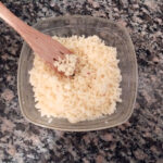 homemade shredded mozzarella cheese in a glass bowl on granite counter