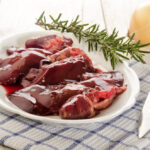 poultry giblets on white plate with rosemary sprig and onion on table