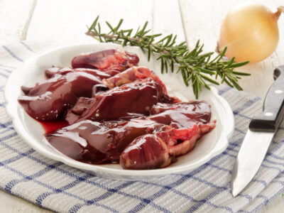 poultry giblets on white plate with rosemary sprig and onion on table