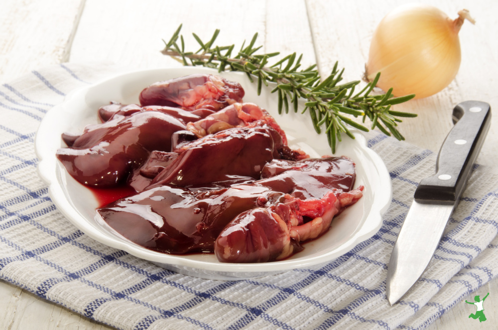 poultry giblets on white plate with rosemary sprig and onion on table